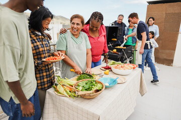 Poster - Multi generational people doing barbecue at home's rooftop - Multiracial friends having fun eating and cooking together during weekend day - Summer and food concept - Main focus on latin woman face