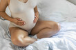 © puhimec - Caucasian pregnant woman touching her belly while sitting on the bed at home.