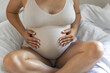 © puhimec - Caucasian pregnant woman touching her belly while sitting on the bed at home.