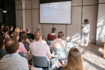 Wall Mural - Group of people engaged in business seminar with speaker presenting. Professional presentation setting with attentive audience and informative slide on screen.