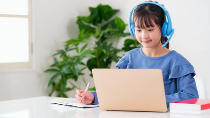 ヘッドホンをつけてノートパソコンで勉強する女の子