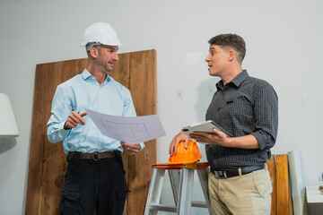 Wall Mural - A Caucasian middle-aged male engineer contractor and an Italian architect engineer are seated at a desk, discussing renovation plans with blueprints and a house model in front of them.