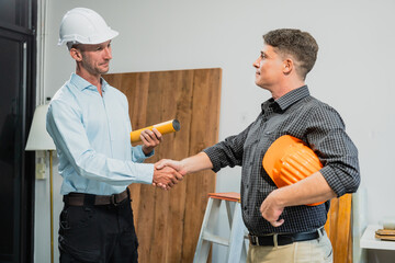 Wall Mural - A Caucasian middle-aged male engineer contractor and an Italian architect engineer are seated at a desk, discussing renovation plans with blueprints and a house model in front of them.