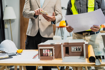 Wall Mural - A Caucasian middle-aged male engineer contractor and an Italian architect engineer are seated at a desk, discussing renovation plans with blueprints and a house model in front of them.