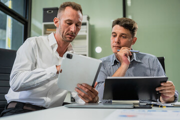 Caucasian middle-aged male businessperson and an Italian accountant are seated at a desk, engaging in a professional meeting, discussing various aspects of technology and innovation in their fields.