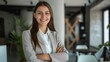 © JINGWEN - Confident businesswoman with crossed arms smiling in modern office, facing camera, embodying success in professional attire with sleek hairstyle.