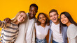 © Prostock-studio - Friendly international students embracing and taking selfie over yellow background