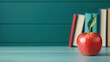 © tonstock - A fresh red apple with a leaf sits on a blue wooden table against a backdrop of colorful books, representing education and healthy living.