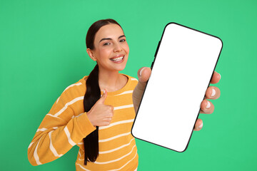 Happy woman showing mobile phone with blank screen on green background. Mockup for design