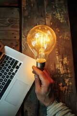 Poster - A person holds a light bulb close to a laptop, possibly for a photo shoot or creative project