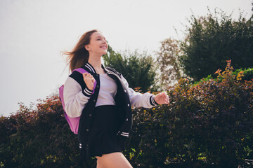 Poster - Photo of attractive excited girl dressed bomber short skirt backpack enjoying wind blowing walking school outdoors urban city park