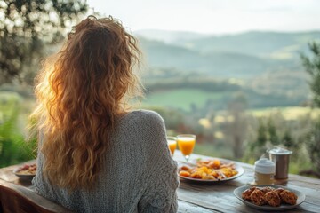 A woman with long red hair is sitting at a table with a plate of food and two glasses of orange juice. The scene is peaceful and relaxing