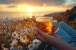 © aiLover - A person is holding a cup of tea while sitting in a field of flowers. The scene is serene and peaceful, with the sun setting in the background