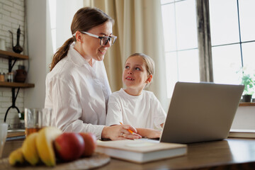 Smiling mother helping daughter with online education at home