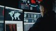 © VK Studio - A man in a control room analyzing multiple screens displaying global data and security information, deeply focused on his task.