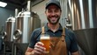 © abu - A proud brewmaster smiles with a freshly poured craft beer in front of brewing equipment, as shiny tanks create an industrial backdrop.
