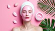 © Inlovehem - A serene woman enjoys a pink facial mask treatment with tropical leaves on a pastel pink background, symbolizing relaxation and skincare.
