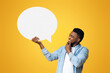 © Prostock-studio - Smiling black millennial guy holding empty speech bubble and touching his chin over yellow studio background, copy space