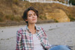 © ViDi Studio - Young happy calm confident beautiful fun European woman she wear shirt casual clothes looking camera sits rest on sea ocean sand shore beach outdoor seaside in summer day free time. Lifestyle concept.