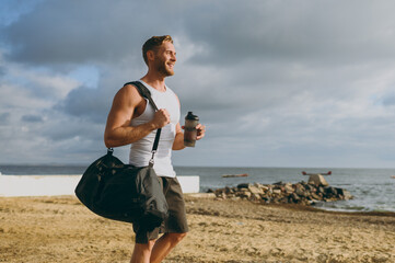 Wall Mural - Sideways young happy strong athletic toned fit sportsman man wear sports clothes bag drink protein shake warm up train at sunrise sun dawn over sea beach outdoor on pier seaside in summer day morning.