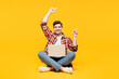 © ViDi Studio - Full body young fun happy IT man he wears red checkered shirt casual clothes sits hold use work on laptop pc computer point finger aside isolated on plain yellow orange background. Lifestyle concept.