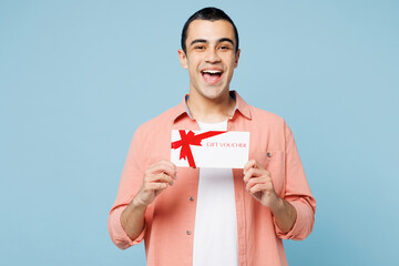 Poster - Young surprised middle eastern man he wear pink shirt white t-shirt hold gift certificate coupon voucher card for store isolated on plain pastel light blue cyan background studio. Lifestyle concept.