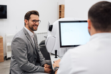 Attractive male doctor ophthalmologist is checking the eye vision of handsome middle age man in modern clinic. Doctor and patient during medical check up in ophthalmology clinic.