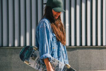 A young woman in a green cap and denim jacket, captured in a candid moment with a skateboard. The graininess and blur add a gritty, urban artistic effect to the photograph.