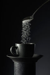 Wall Mural - Sugar is poured into a black cup of coffee on a black background.