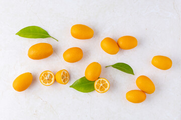 Wall Mural - Sweet and sour kumquat, fresh raw whole and sliced citrus fruits with leaves on light marble table background.