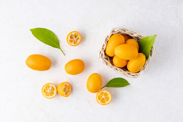 Wall Mural - Sweet and sour kumquat, fresh raw whole and sliced citrus fruits with leaves on light marble table background.