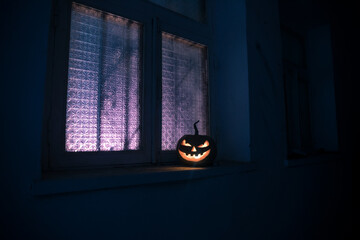 Scary Halloween pumpkin in the mystical house window at night or halloween pumpkin in night on room with blue window. Symbol of halloween in window. Selective focus