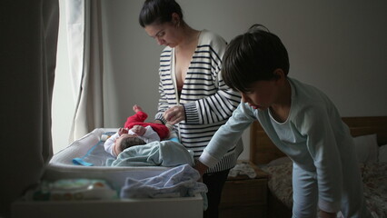 Mother and young sibling engage in caring for a newborn baby on a changing table, highlighting a warm family interaction and bonding moment in a home setting