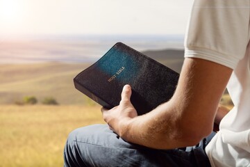 Poster - Bible in human hands in nature background, Christian concept.