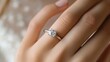 © Nathan - A close-up of a woman's hand showcasing an elegant diamond engagement ring with a classic design.