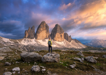 Wall Mural - girl with backpack on the stone and high mountain peaks at colorful sunset in summer. tre cime, dolo