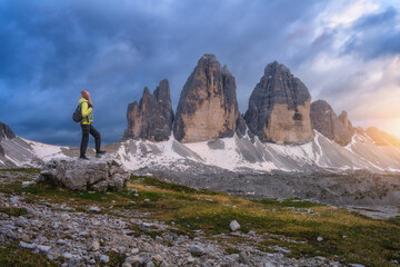 Wall Mural - girl with backpack on the stone and high mountain peaks at colorful sunset in summer. tre cime, dolo