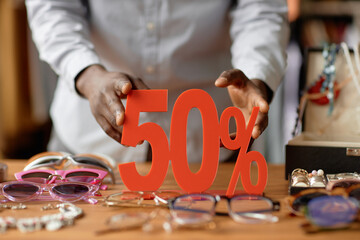 Wall Mural - Close up on hands of African American salesman setting fifty percent discount red sign on wooden display table cluttered with vintage sunglasses and fashion accessories at second hand shop, copy space