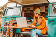 © MVProductions - Young woman digital nomad engaging in remote work outside her vintage camper van, epitomizing the mobile, van life lifestyle