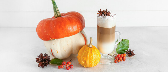 Wall Mural - Glass cup of tasty pumpkin latte with star anise and viburnum on white table