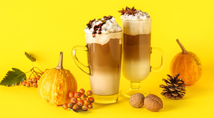 Wall Mural - Glass cups of tasty pumpkin latte with star anise, walnuts and viburnum on yellow background