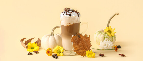 Poster - Glass cup of tasty pumpkin latte with star anise and beautiful flowers on yellow background