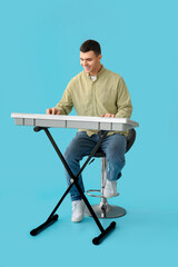 Wall Mural - Young man playing synthesizer on blue background