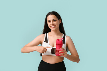 Wall Mural - Beautiful young happy woman pointing at sports bottle of water on blue background