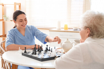 Wall Mural - Physical therapist with senior woman playing chess at table in kitchen