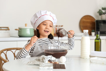 Funny little Asian girl whisking melted chocolate in kitchen