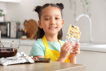 Poster - Cute little Asian girl with white chocolate bar in kitchen