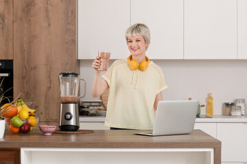 Canvas Print - Sporty young woman with glass of fruit smoothie and blender in kitchen