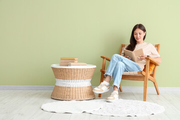 Wall Mural - Beautiful young woman reading book and sitting on armchair at home