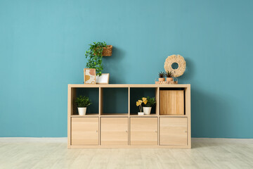 Canvas Print - Wooden chest of drawers with photo frames and houseplants near blue wall